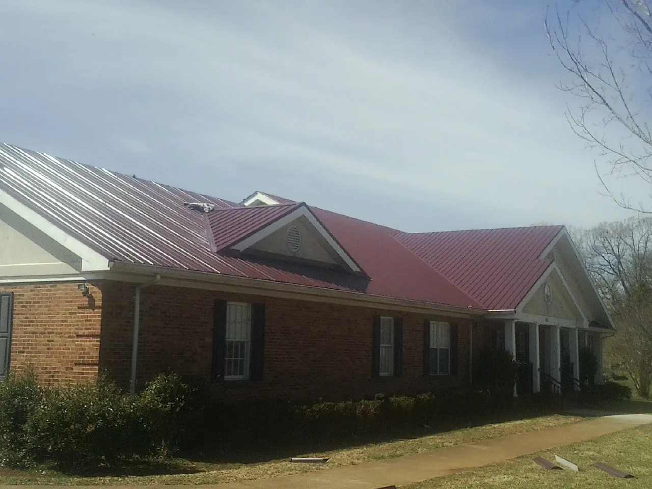 Red metal roof with gabled entries on a long brick building, from a Hail Damage Roof Repair job in Sekiu