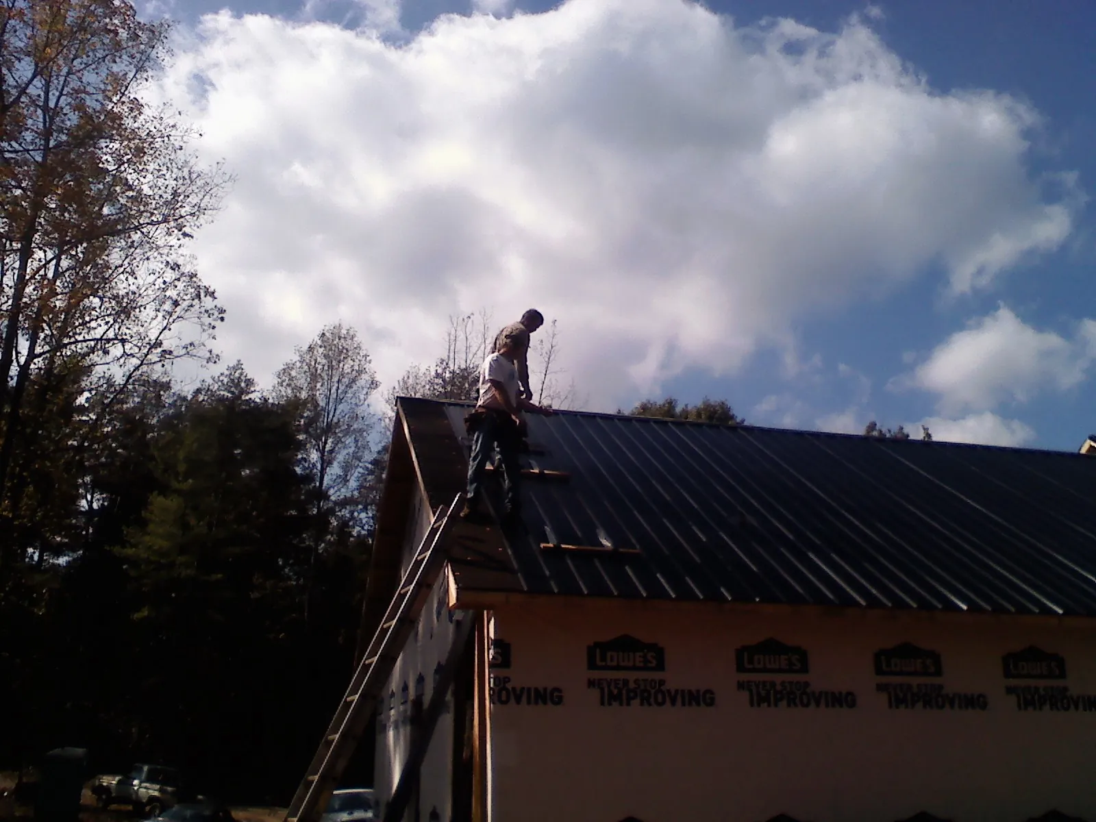 Roofer fastening dark metal panels high against a cloudy sky, from a Roof Inspection job in Sekiu