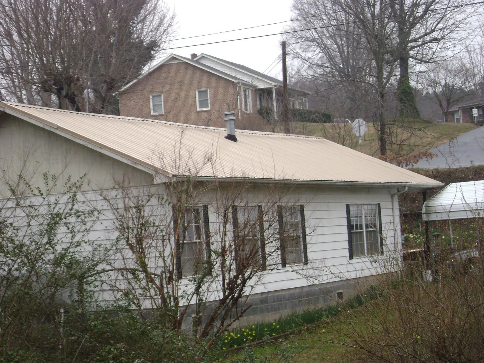 Tan metal roof on a white sided house set into a hillside — Commercial Roofing by Roofing Brothers in Sekiu